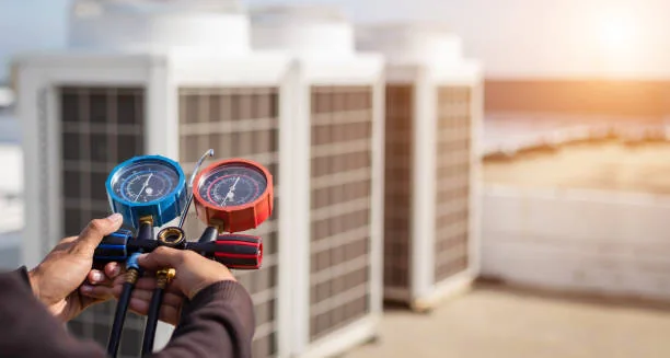 Technician holding a refrigerant manifold gauge set beside outdoor units
