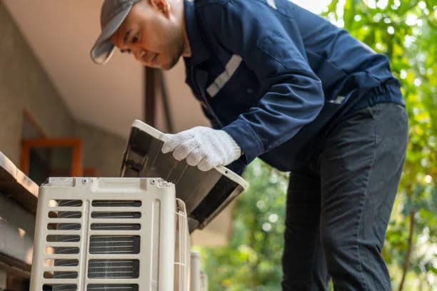 Technician in gloves lifting the access panel off an outdoor unit during a tune-up