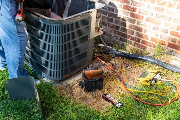Technician working on an outdoor condenser with tools and meters laid out on the grass